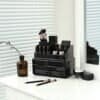 Sort makeup organizer med børstepensler, neglelak og kosmetik på bord.