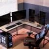 Hjørnecomputerbord med tre skærme, gamingstol og gamingudstyr.