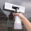 Hand holder en elektrisk vinduesvisker med sprayflaske til rengøring af bilruder.