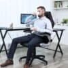 Mand sidder i ergonomisk kontorstol, drikker kaffe og arbejder ved skrivebord.
