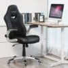 Sort ergonomisk kontorstol med foldede arme foran computer på skrivebord.
