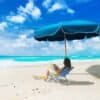 Grøn strandstol med parasol på sandstrand ved havet.