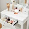 Hvid makeup bord med spejl, lys, makeup produkter og skuffer.